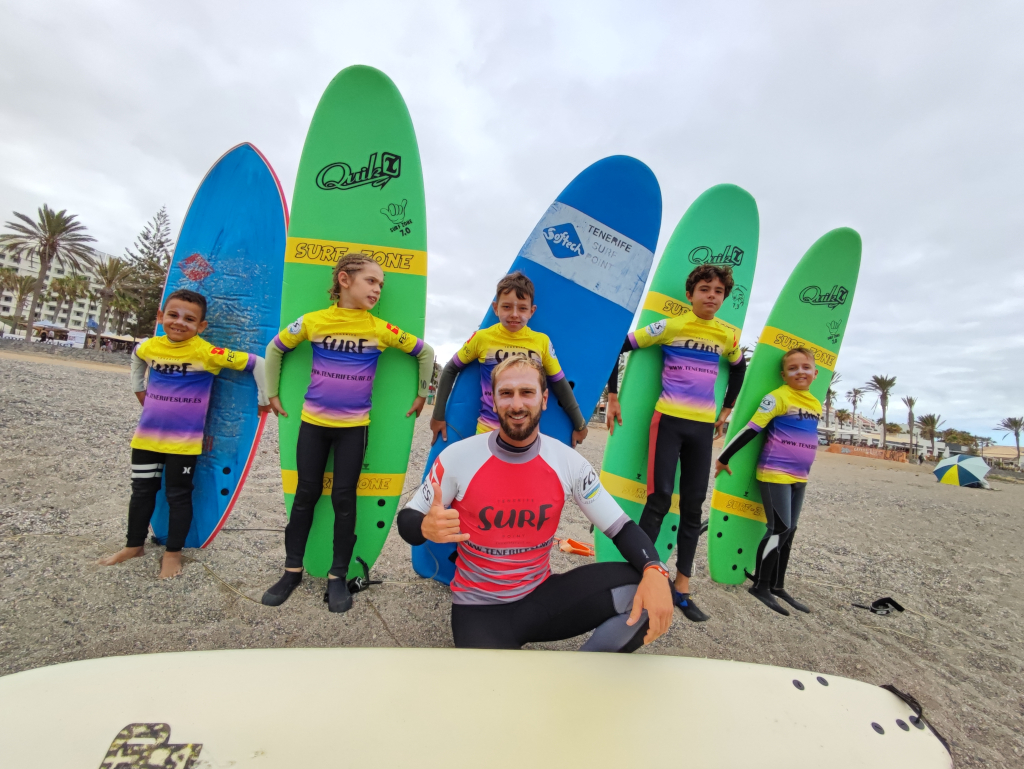 Surf instructor with children holding boards on Tenerife beach.