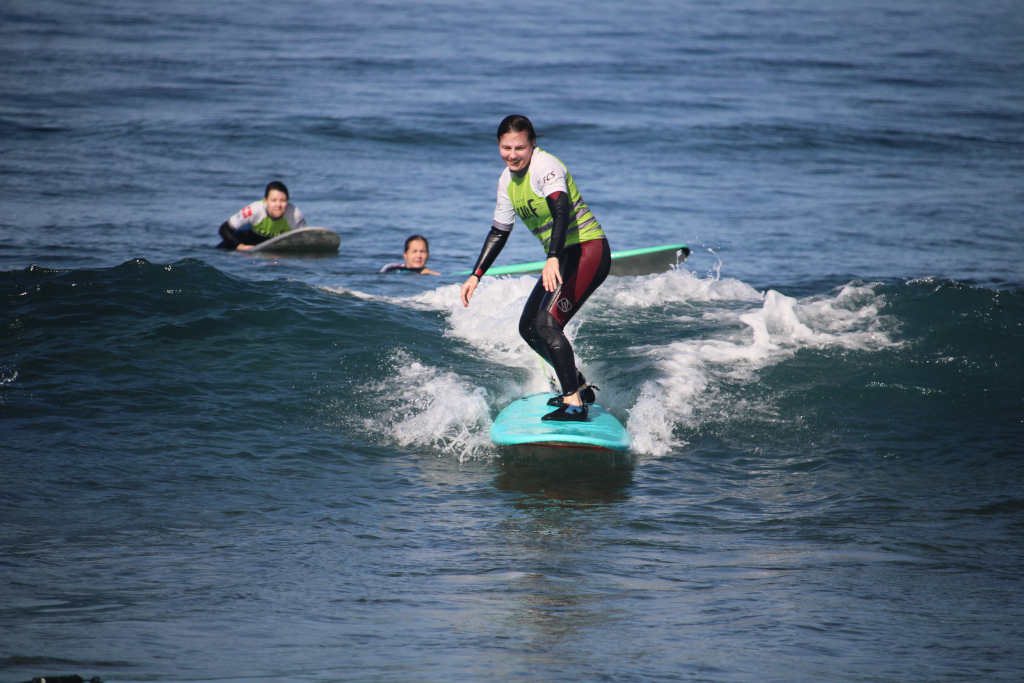 Surfer riding a wave in Punta del Hidalgo, Tenerife, with two people in the background.