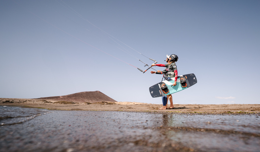 Person practicing kitesurfing in Playa El Médano, Tenerife, with a hill in the background.
