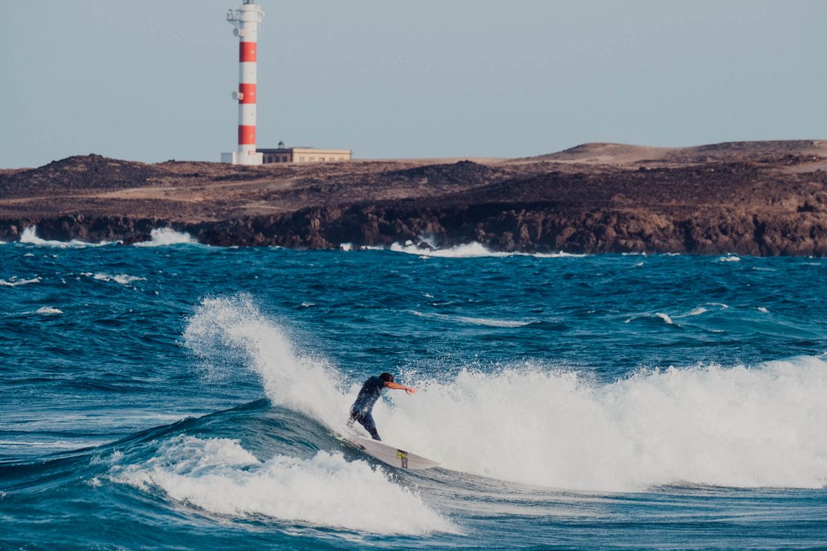 Surfer riding a wave in front of the lighthouse in Punta de Hidalgo, Tenerife.