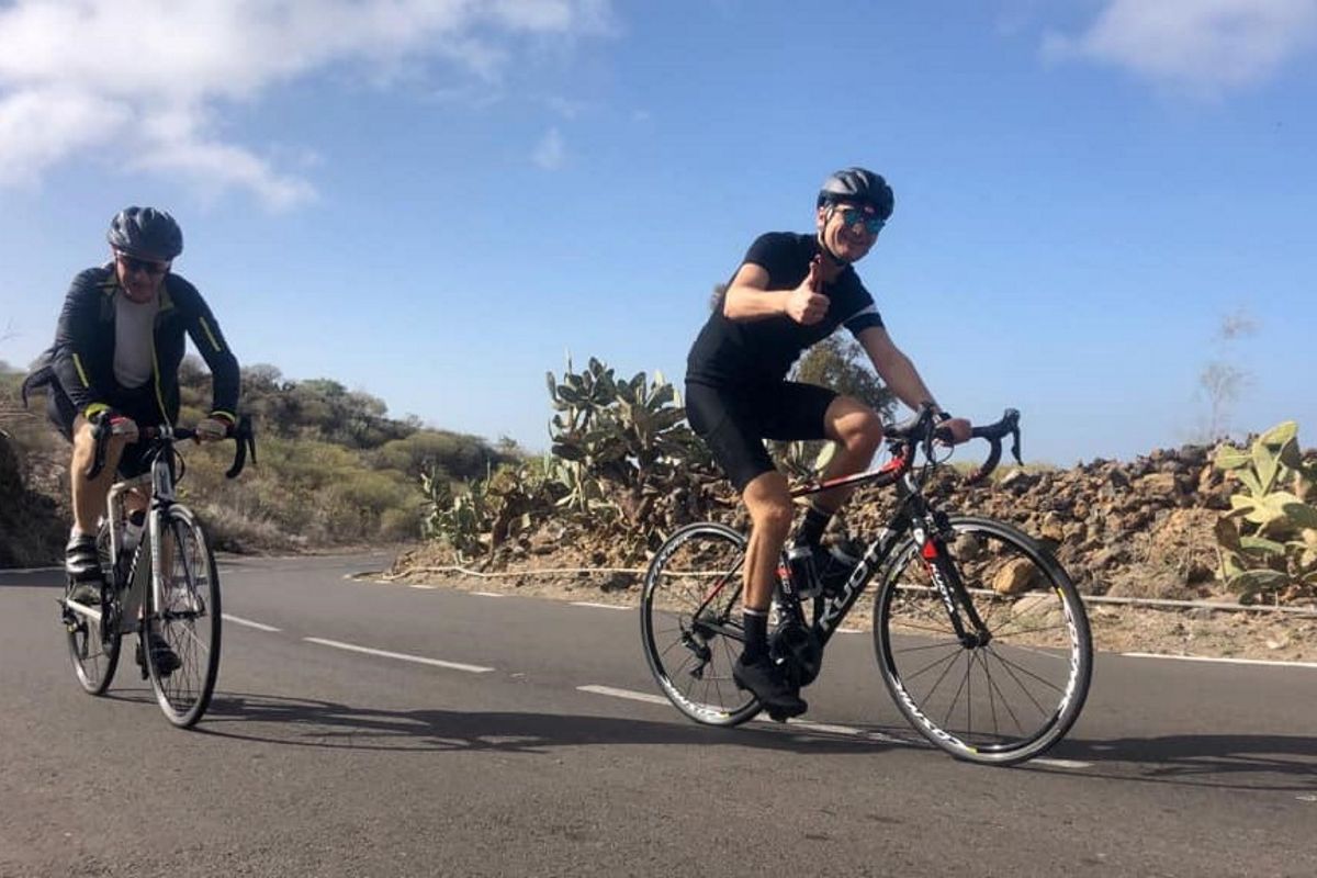 Cyclists on the road near cactus in Tenerife under clear skies.