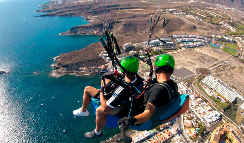 People paragliding over the coast of Tenerife with aerial view of the sea and buildings.