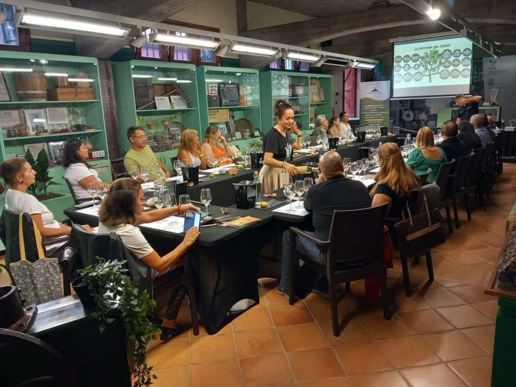 People at a wine tasting in a decorated room in Tenerife. Visible text: The Anatomy of Cocoa.