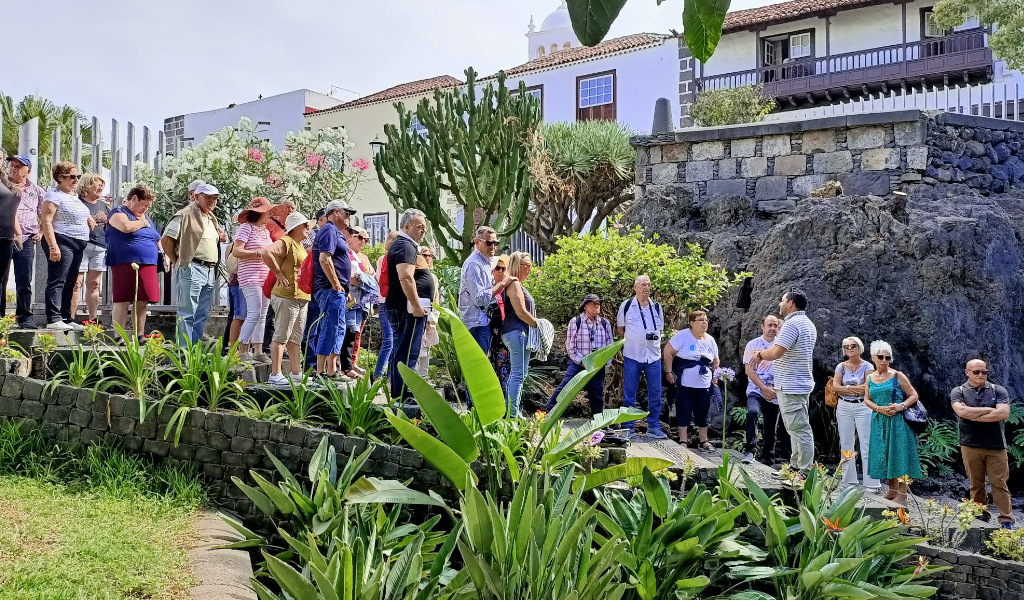 Group of people walking through a garden in a place in Tenerife, surrounded by plants and local architecture.