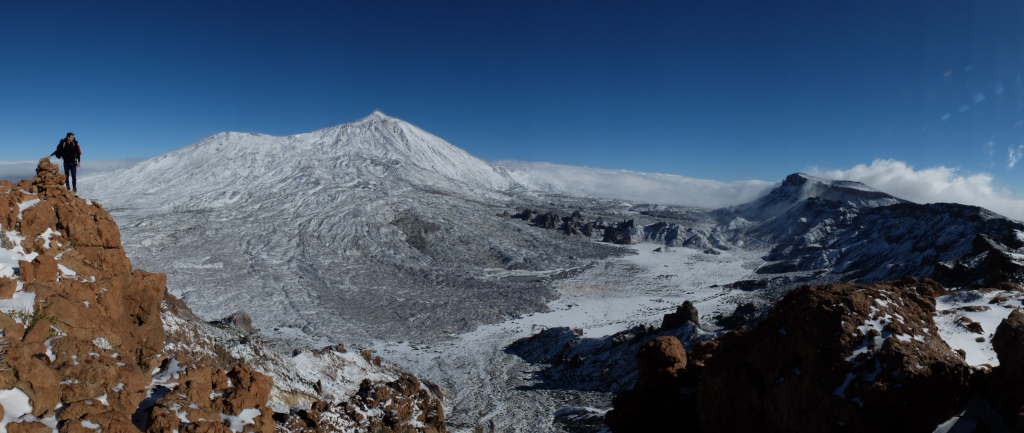 Snowy landscape of Mount Teide in Tenerife with a hiker on top of a rock.