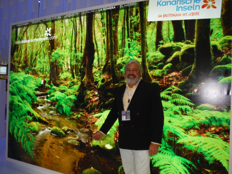 Man in front of a promotional poster of La Gomera and hallokanarischeinseln.com.