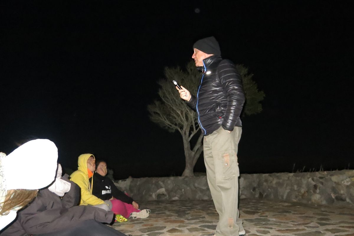 Person talking outdoors at night in Tenerife, with group sitting nearby.