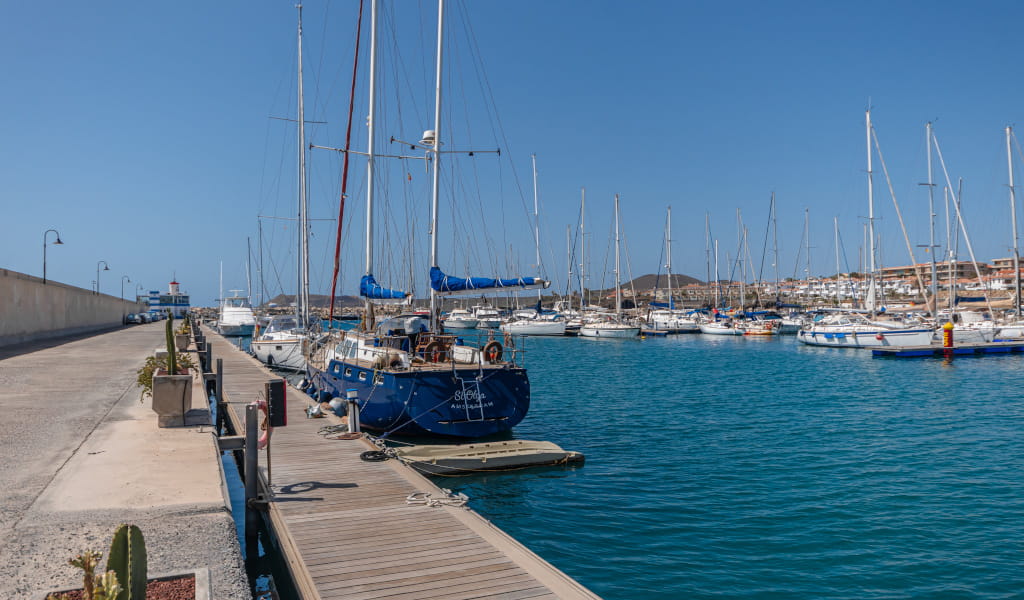 Boats moored in the port of Las Galletas, Tenerife, with a lighthouse in the background.