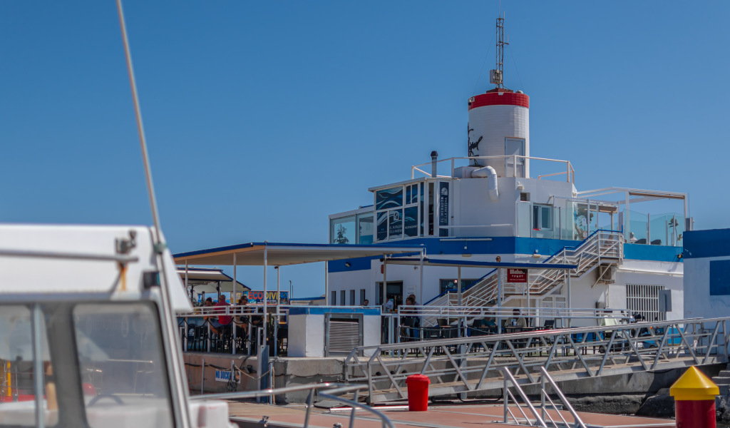 White and blue building with red lighthouse in Santa Cruz de Tenerife, seen from a pier.