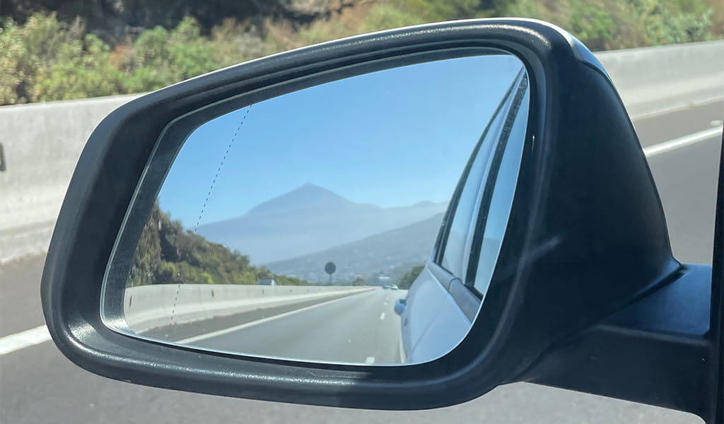 Reflection of Mount Teide in the rearview mirror of a car on the road in Tenerife.
