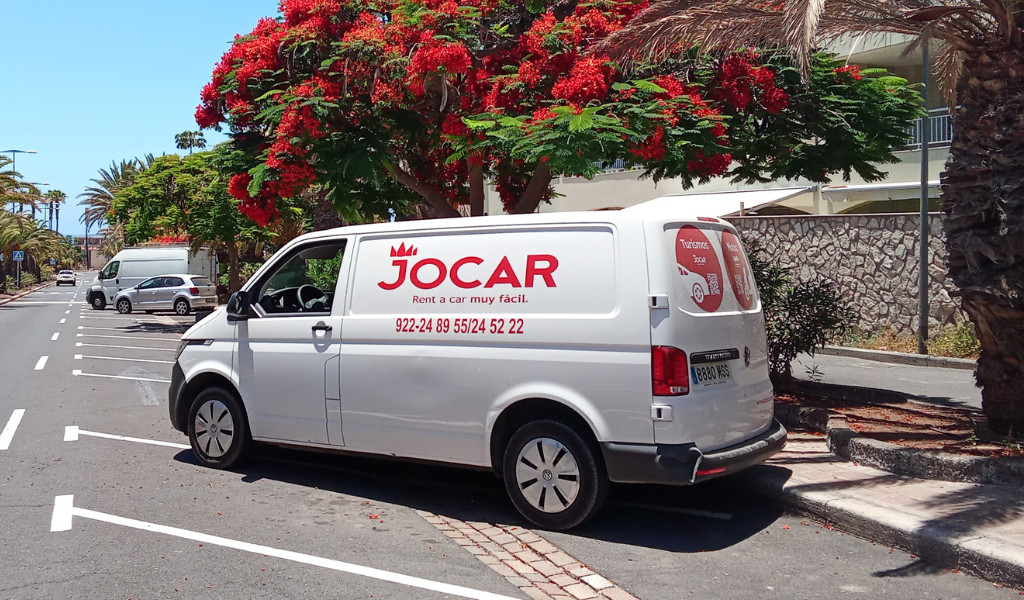 Jocar rental van in Santa Cruz de Tenerife parked next to a tree with red flowers.