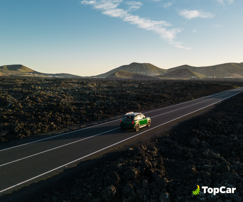 Green car driving on the road between volcanic landscapes in Tenerife. TopCar logo.