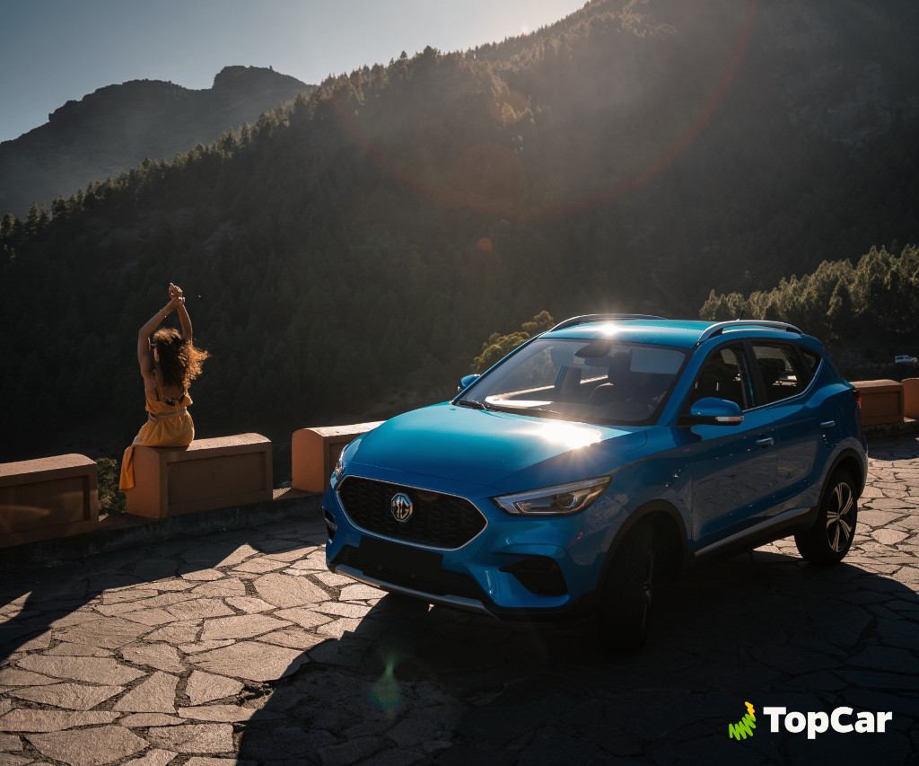 Blue car in front of mountains in Tenerife, woman sitting on wall under the sun.