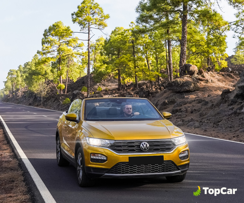 Yellow car on road surrounded by pine trees in Tenerife. TopCar logo.