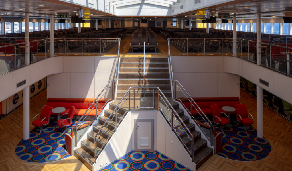 Indoor lounge of a ferry in Tenerife with red chairs and tables.