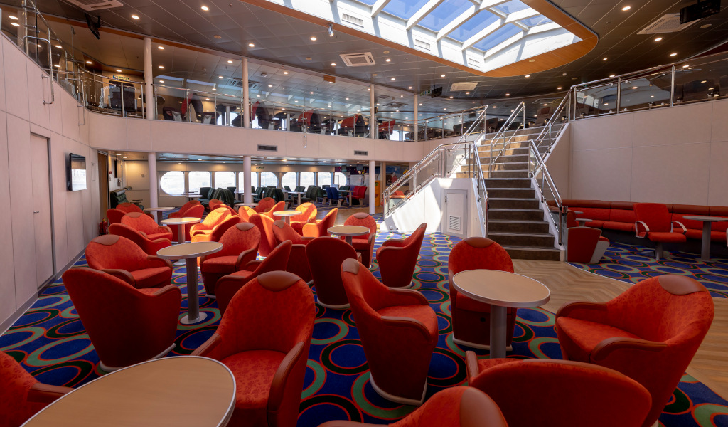 Indoor lounge of a ferry near Tenerife with red chairs and stairs.