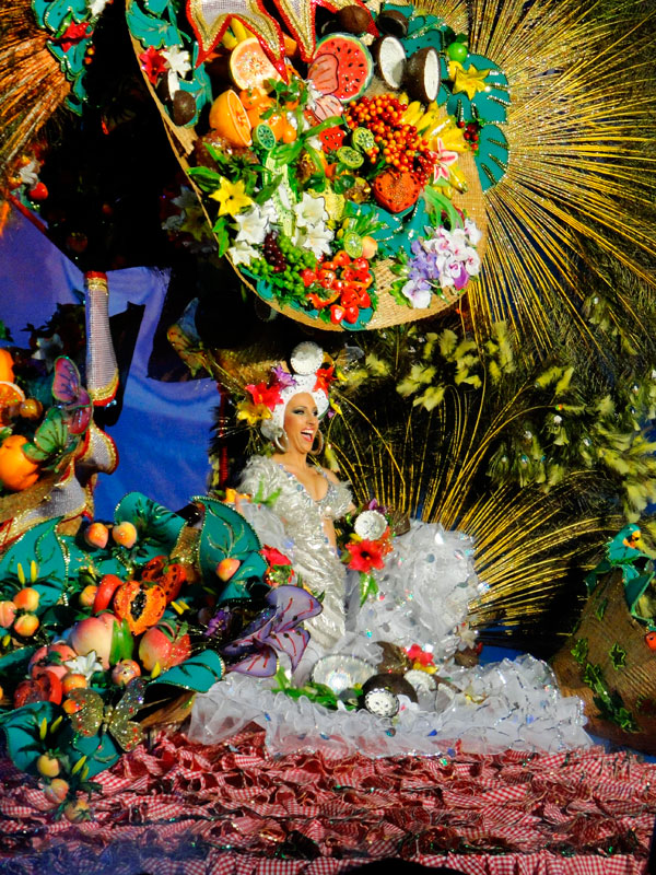 Smiling person in colorful fruit and flower costume, participating in the Tenerife Carnival.
