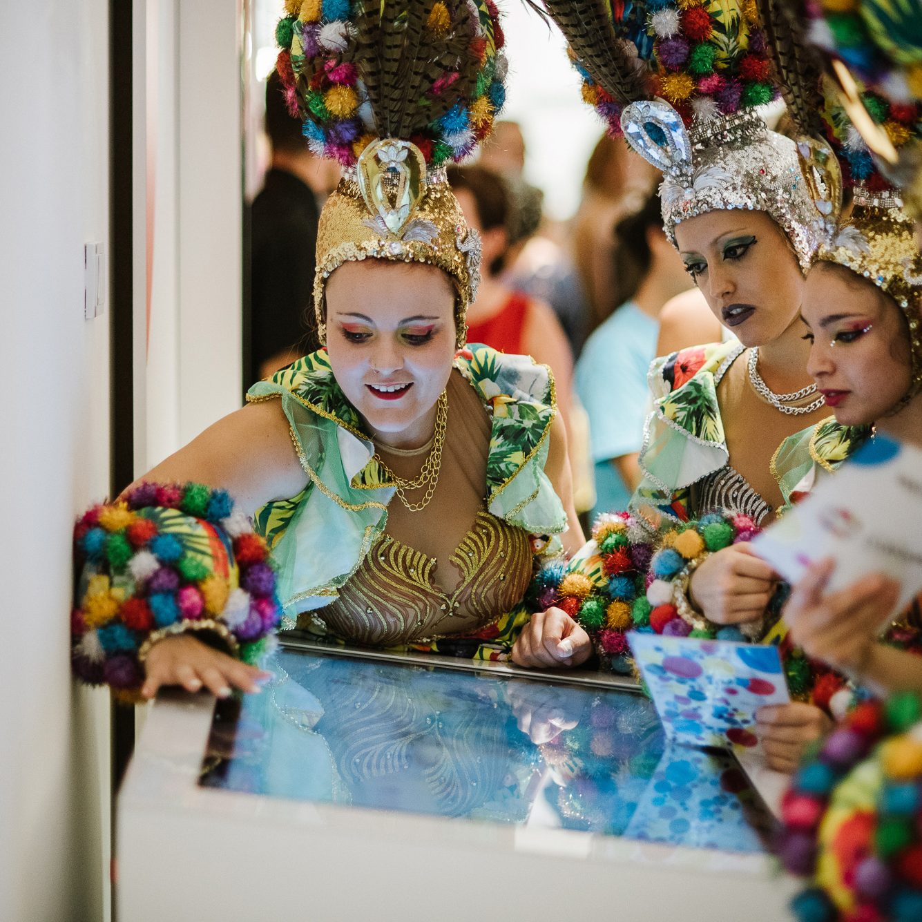 People in colorful carnival costumes interact with a touch screen in Tenerife.