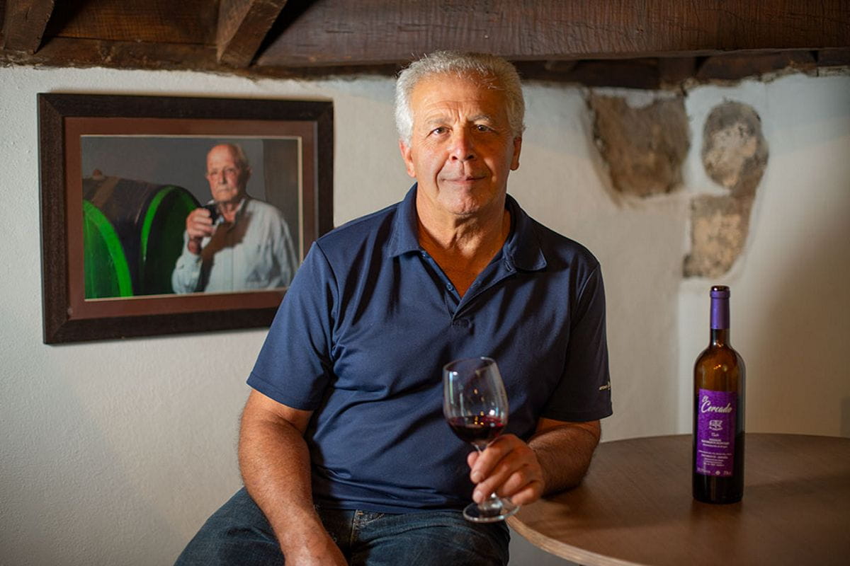 Man holding glass of wine next to bottle and portrait in Tenerife cantina.