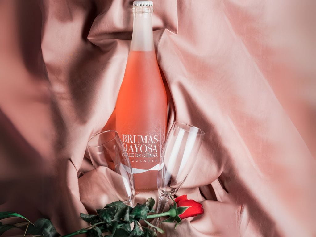 Bottle of Brumas De Ayosa Valle de Güímar sparkling wine with glasses and red rose.
