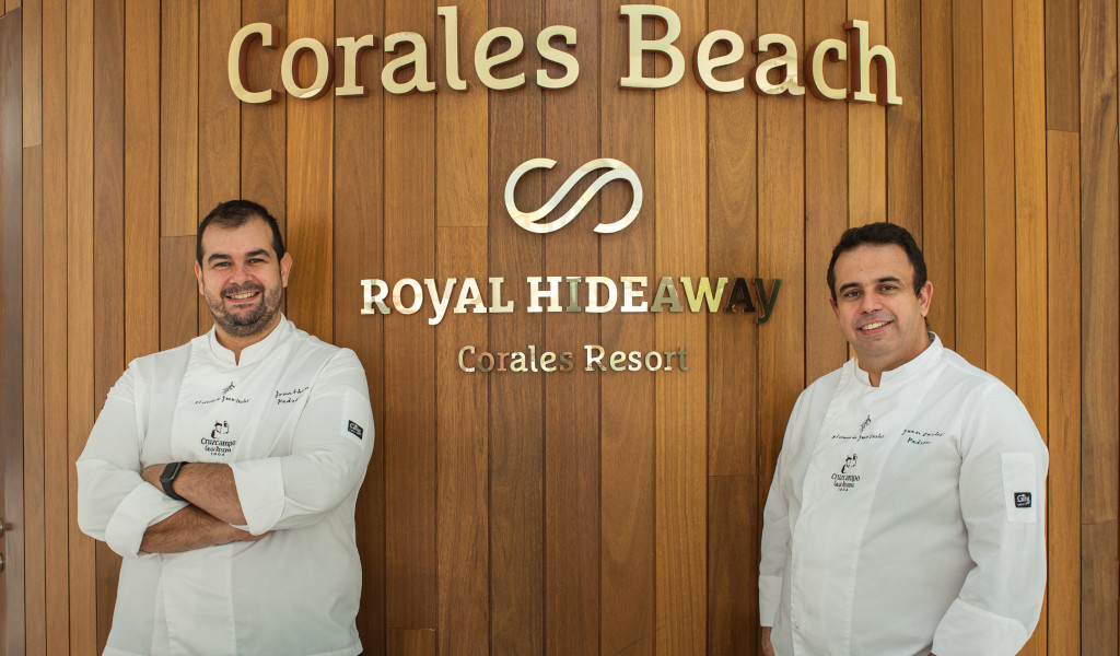 Two chefs in front of the Corales Beach Royal Hideaway Corales Resort sign.