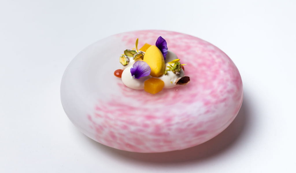 Gourmet dessert with cream, mango and edible flowers on a pink plate in Tenerife.