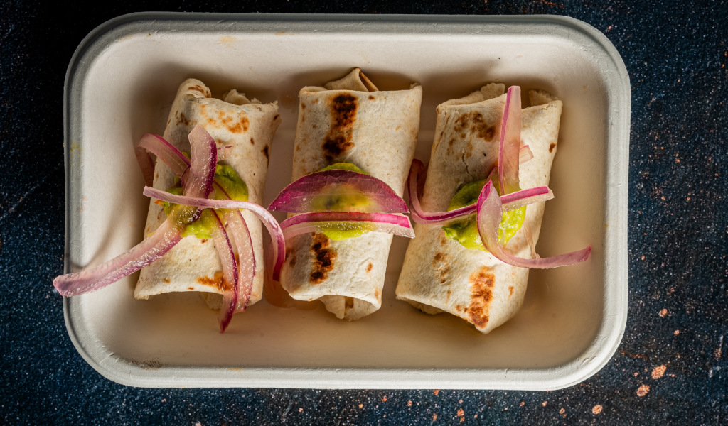 Three burritos with red onion and salsa verde on a rectangular plate in Tenerife.