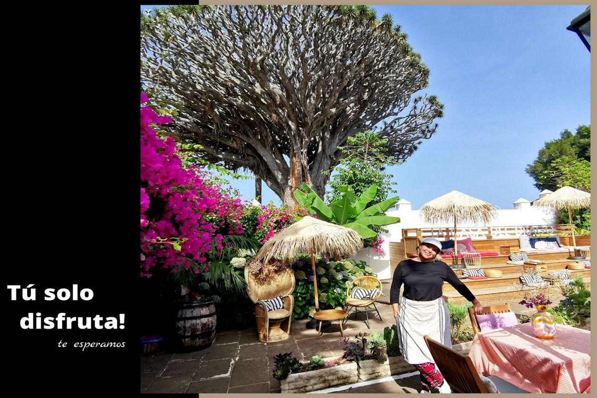 Patio with vegetation, straw umbrellas and one person in Tenerife. Text: You just enjoy! We are waiting for you.