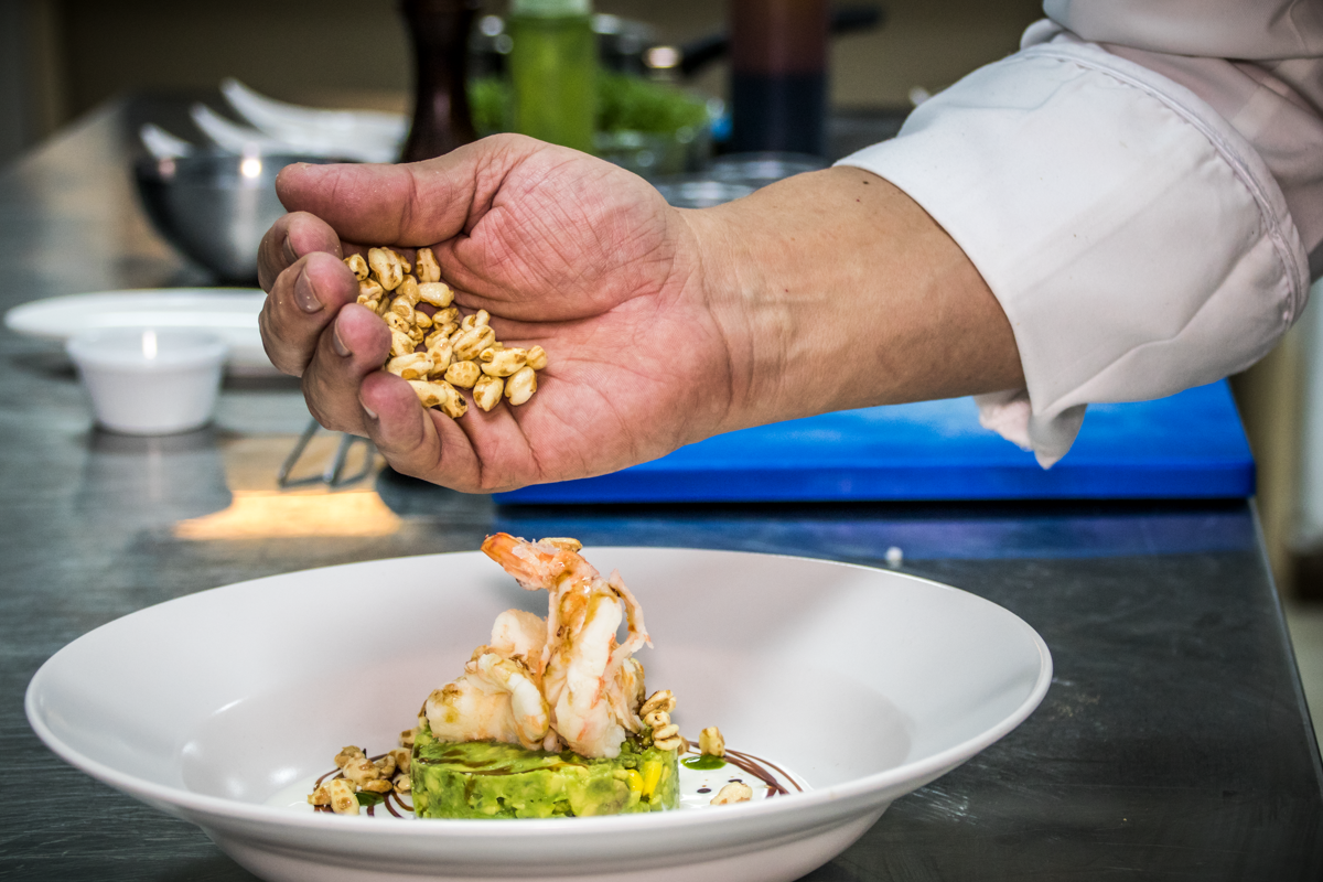 Chef's hand adding grains to a dish with shrimp and avocado in Tenerife.
