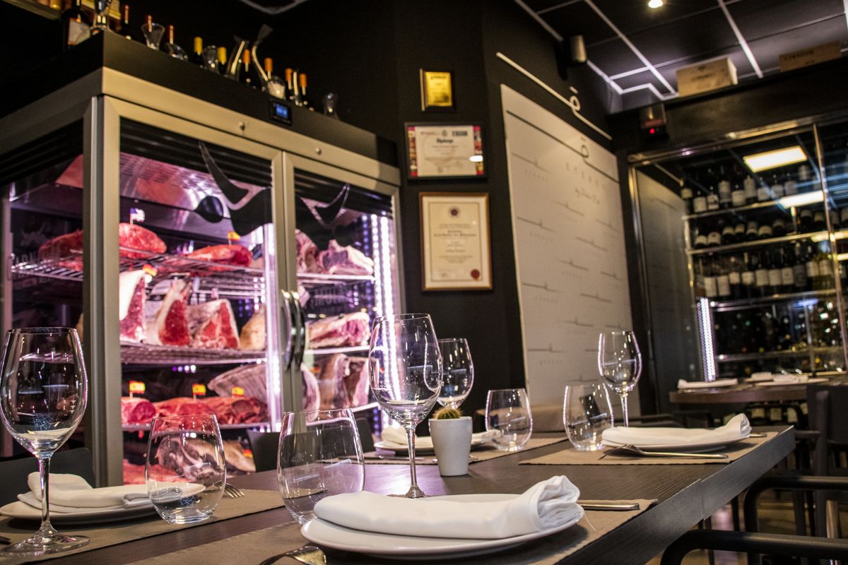 Table with wine glasses, folded napkins and refrigerator with meats in a restaurant in Tenerife.