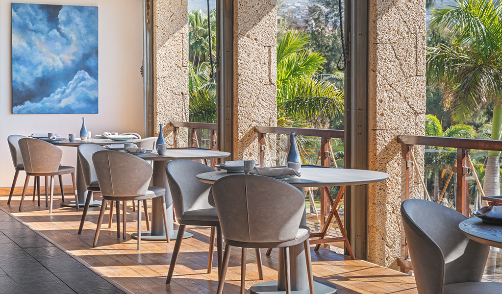 Dining room with tables and chairs next to large windows overlooking gardens in Tenerife.