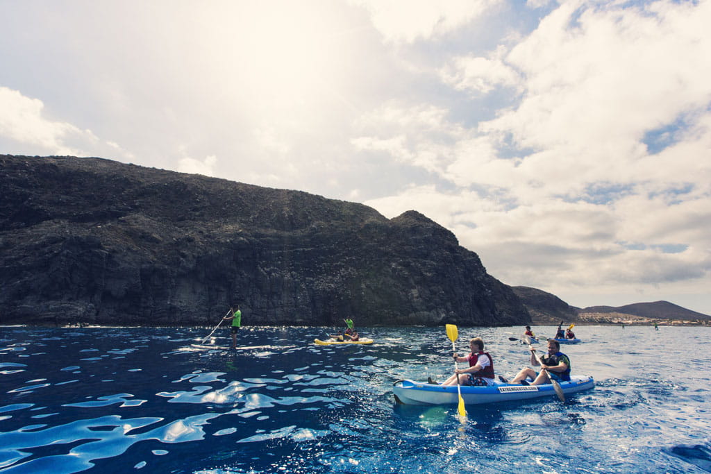 People kayaking and paddle surfing on the coast of Tenerife with mountains in the background.