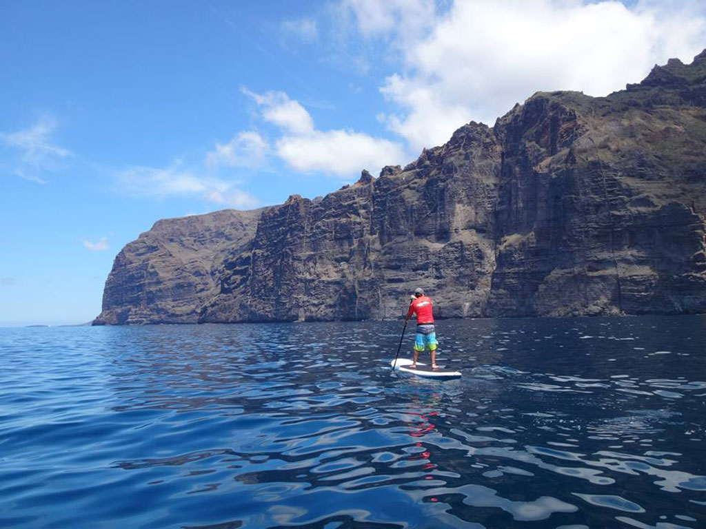 Person paddle surfing in front of the cliffs of Los Gigantes, Tenerife.