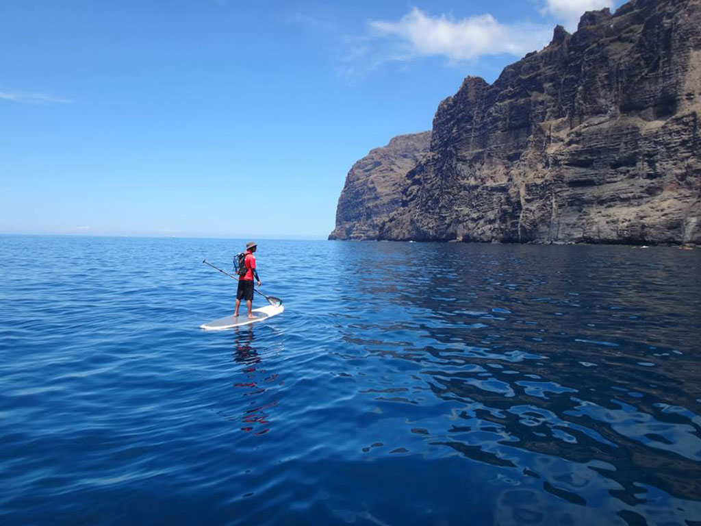 Person paddle surfing in front of the cliffs of Los Gigantes, Tenerife.