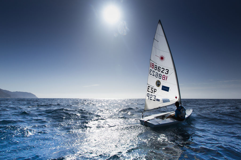 Person sailing on a sailboat under bright sun near the coast of Tenerife.