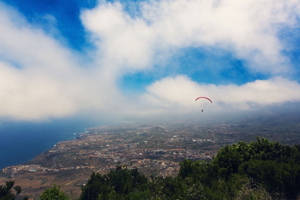 Paragliding flying over the coastal landscape of Tenerife under a partly cloudy sky.