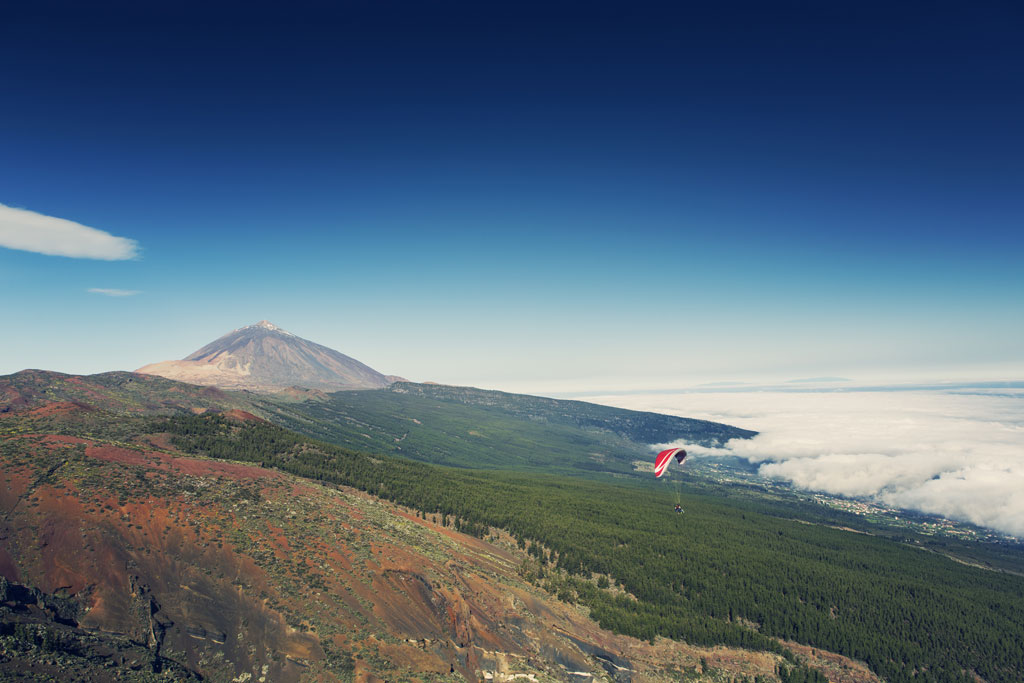 Paragliding over Mount Teide in Tenerife, with clouds and volcanic landscape.
