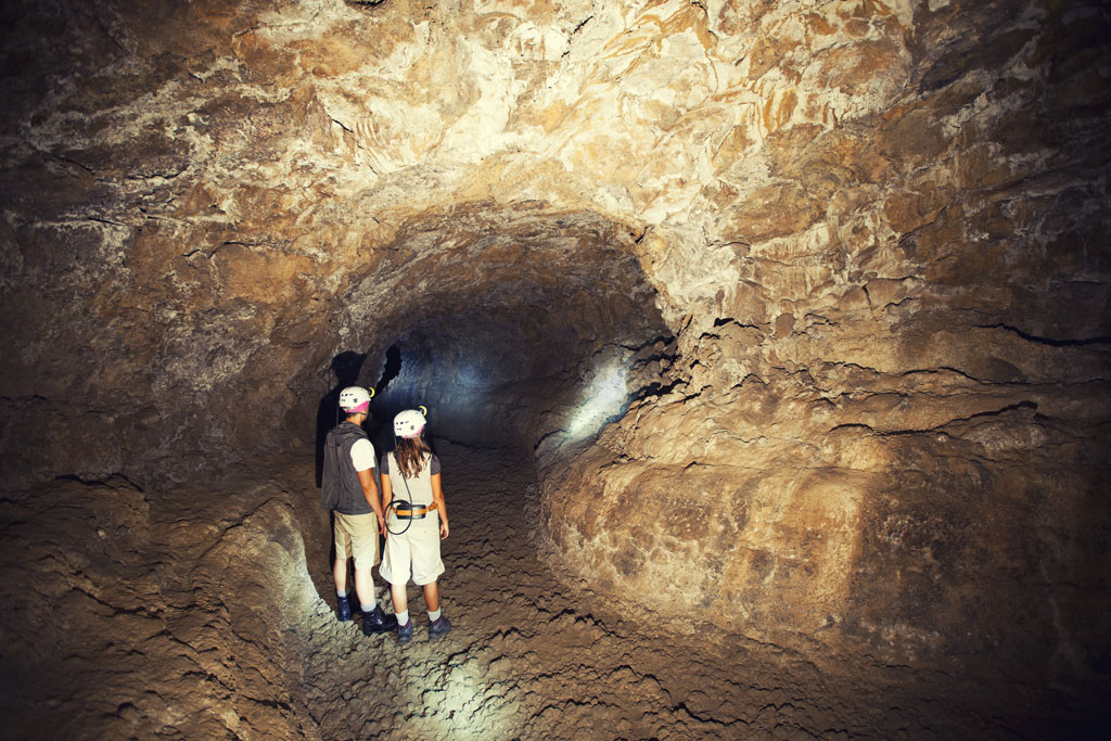 Explorers wearing helmets walk through a tunnel in Cueva del Viento, Tenerife.