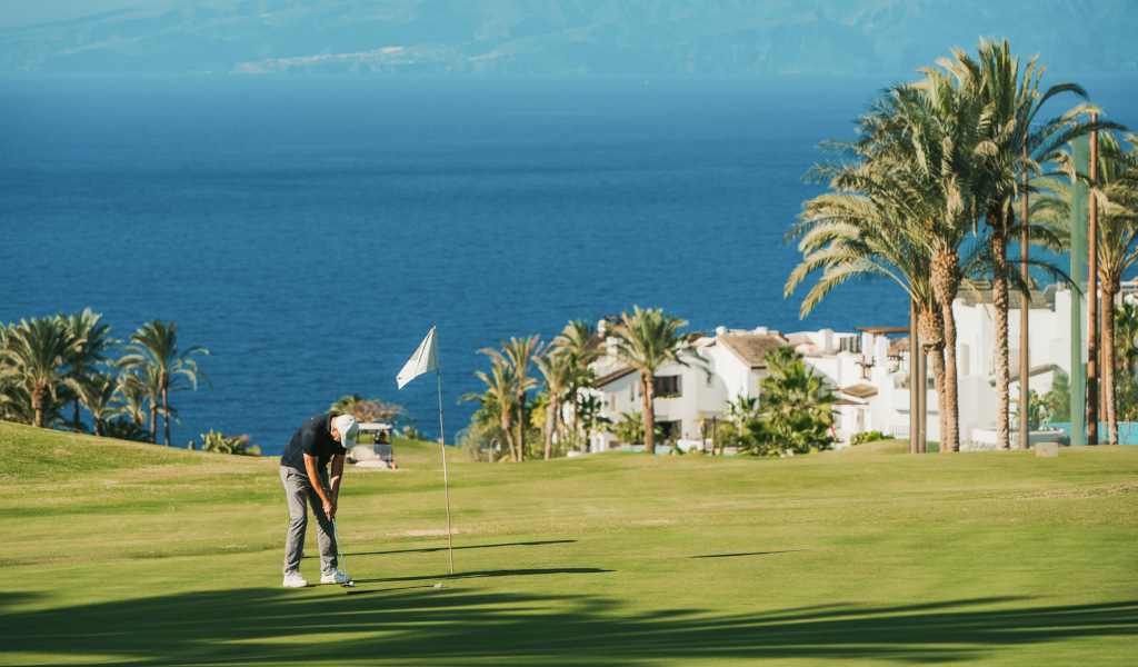 Person playing golf on a course with sea views and houses in Tenerife.