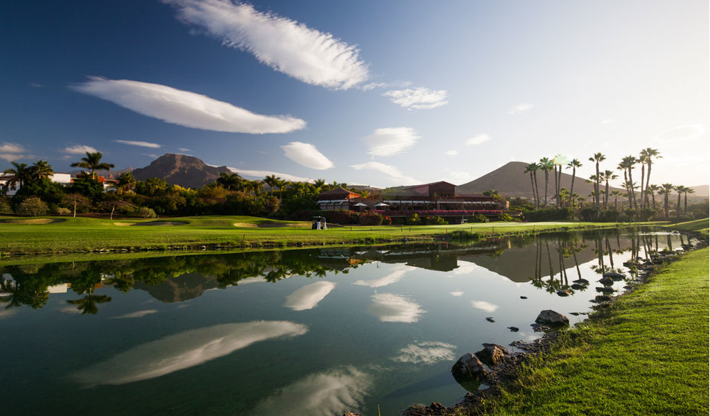 Golf course with mountains and palm trees reflected in a lake in Tenerife.