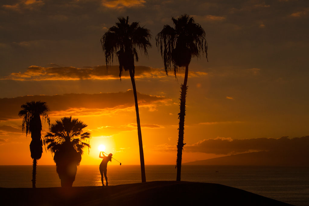 Sunset with palm trees and person playing golf in Tenerife.