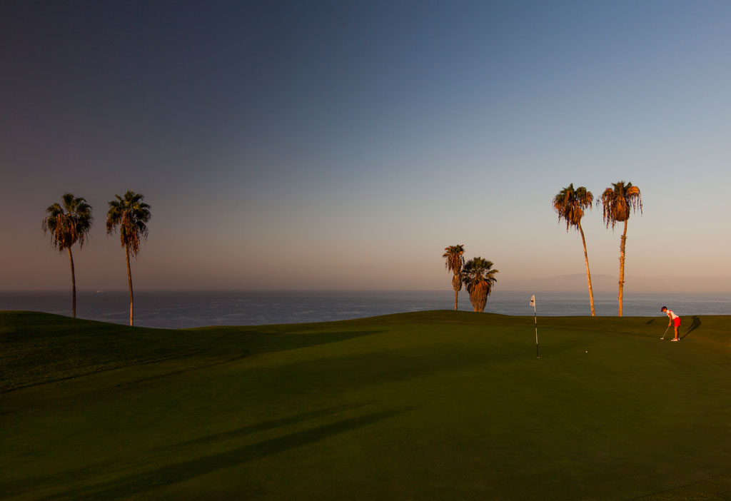 Golf course at sunset with palm trees and player in Tenerife.