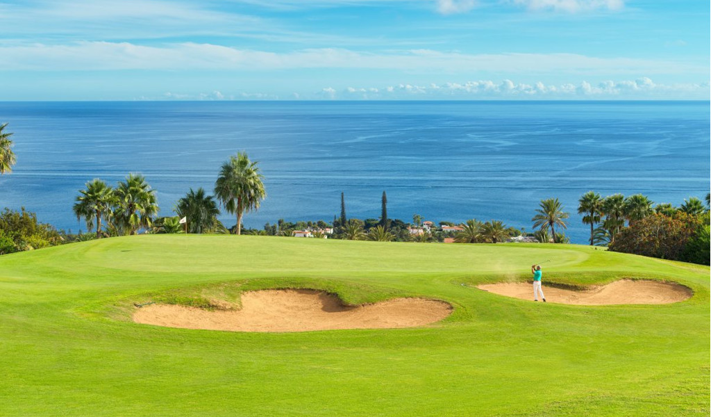 Golf course in Tenerife with ocean view. Blows near bunkers surrounded by palm trees.