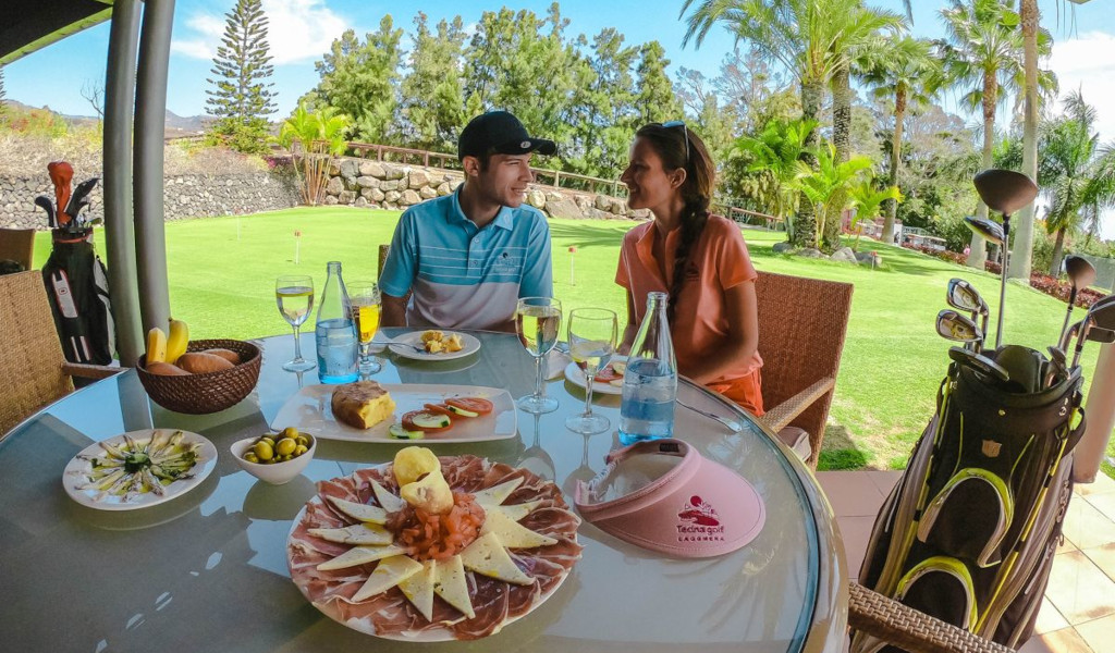 Couple sitting with food and golf clubs at Tecina Golf, La Gomera, Tenerife.