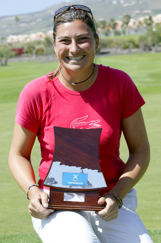 Smiling person holds golf trophy with Tenerife logo on a golf course.