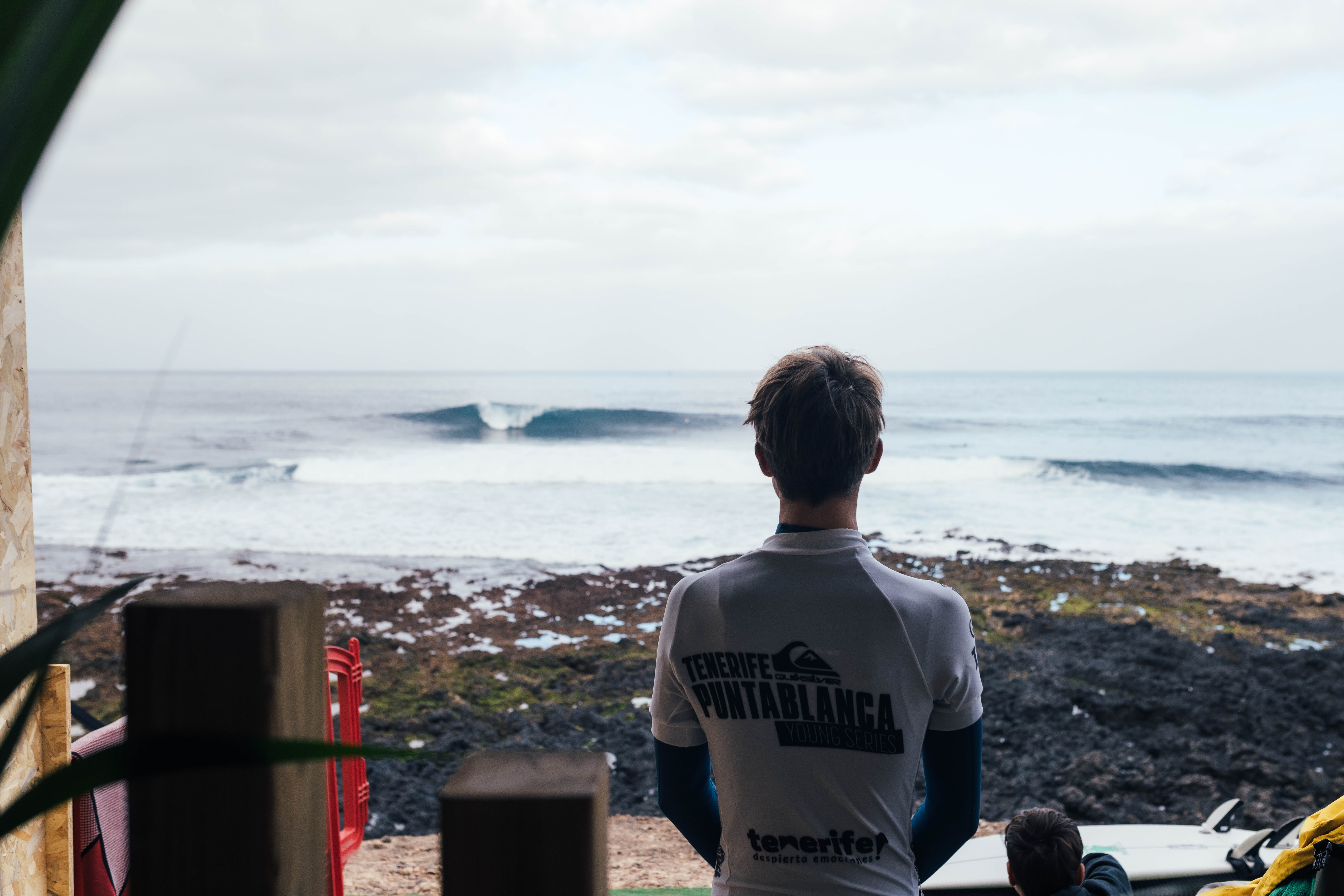 Surfer watches the waves in Punta Blanca, Tenerife, wearing a competition shirt.