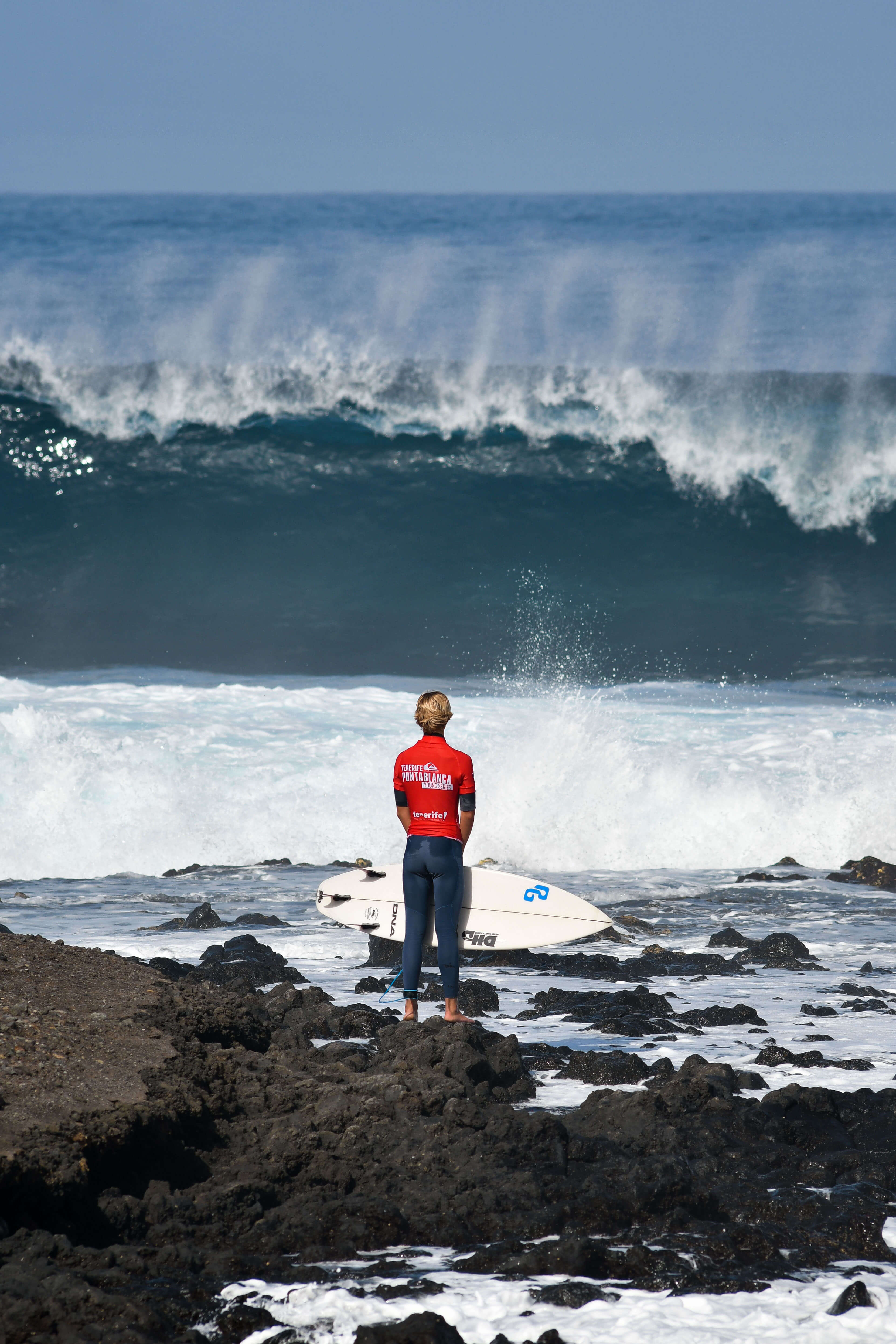 Surfer standing with a board in front of big waves in Punta Blanca, Tenerife.