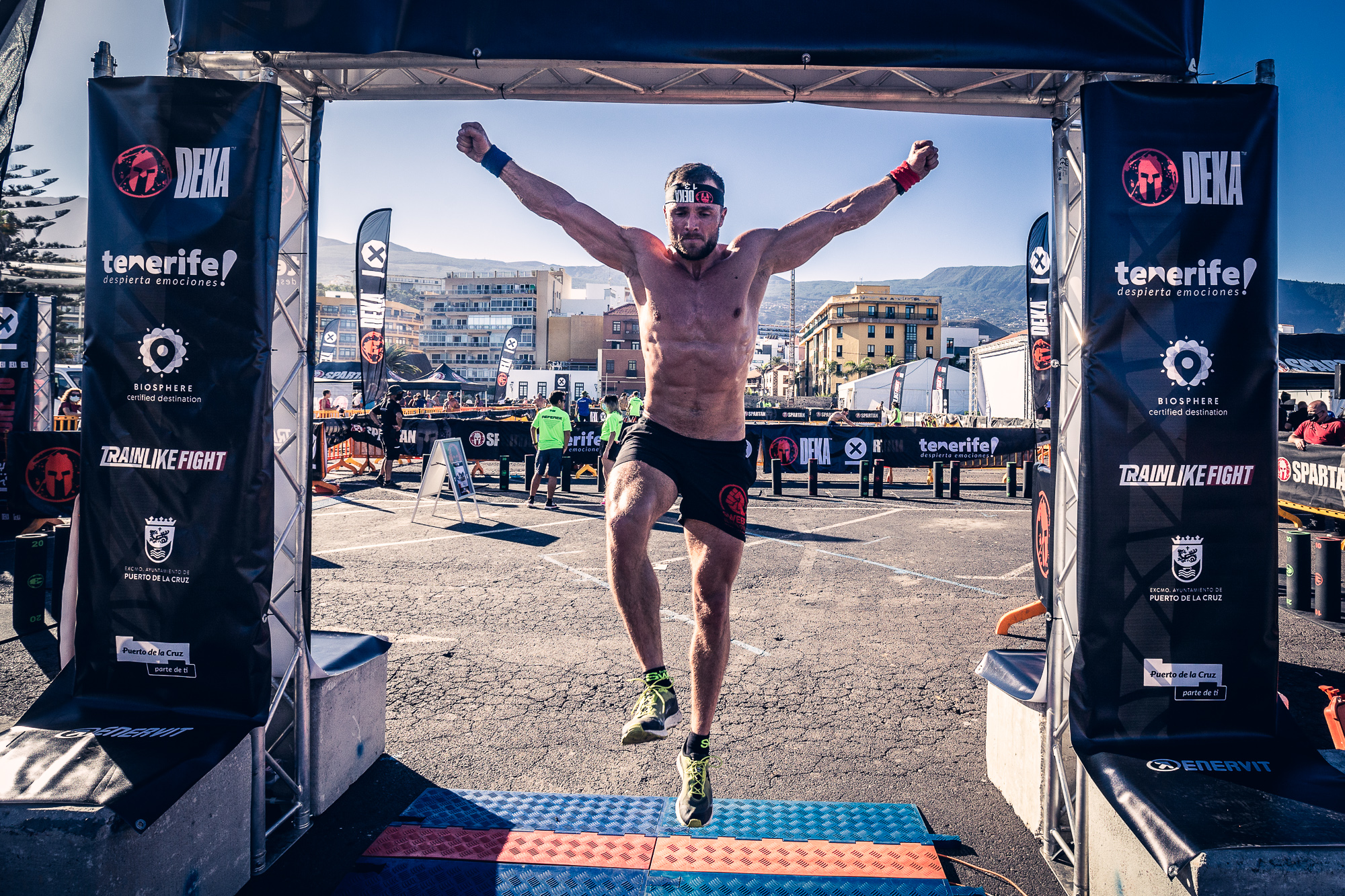 Athlete crossing the finish line in Tenerife competition, with banners and urban background.