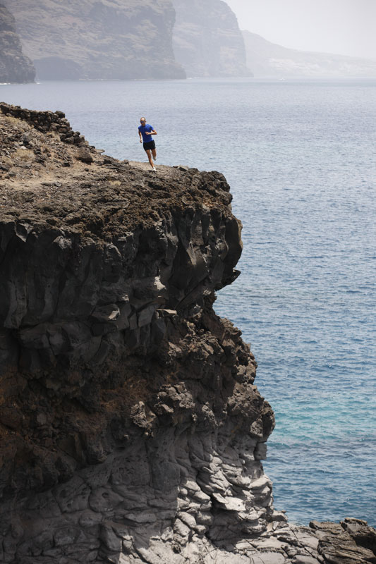 Person running on a cliff in Los Gigantes, Tenerife, with the ocean in the background.