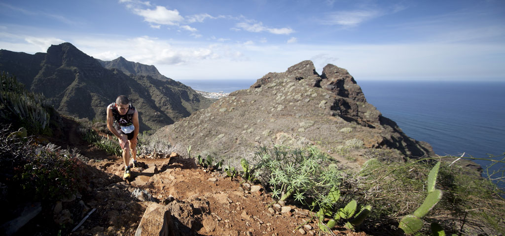 Person climbing hill with sea and mountain views in Tenerife.